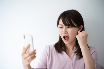 Angry business woman talking on smart phone against white wall