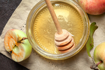 A jar of honey closeup and ripe garden striped apples on a beige napkin and a dark textured background