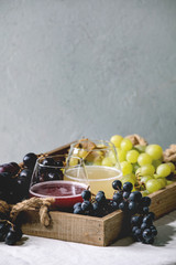 Traditional New european low alcohol red and white wine Federweisser or Neuer Wein, Burcak, Vin bourru in glasses with black and green grapes bunches in wooden tray on white table cloth. Copy space.