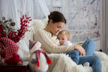 Mother breastfeeding her toddler son sitting in cozy armchair, wintertime.