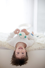 Cute portrait of child upside down, lzing on bed, smiling at camera