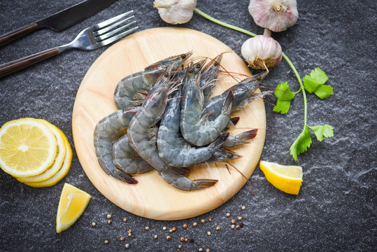raw shrimps on wooden cutting board plate - fresh shrimp prawns for cooking with spices lemon on dark background in the seafood restaurant