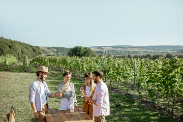 Group of young friends dressed casually tasting wine on the vineyard on a sunny summer morning,...
