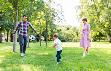 Fototapeta premium family, leisure and people concept - happy mother, father and little son with ball playing soccer at summer park