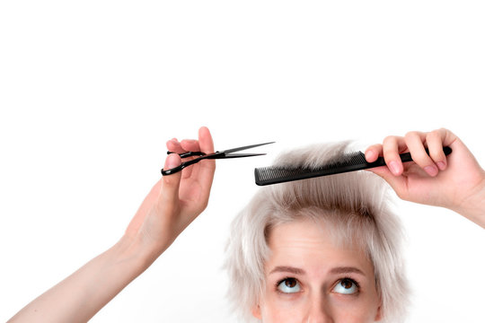Close-up photo of a pretty young blond hairdresser cutting hair herself expressing emotion of  doubt. Beauty industry and professional career. Don't do it yourself, trust professionals.