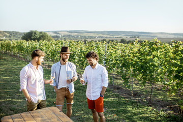 Three guys dressed casually tasting wine while spending time together on the vineyard on a sunny summer morning