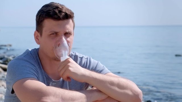 Portrait sick man uses nebulizer on seaside. Inhaling inhaler mask. Fibrosis cystic copd and treatment inhaler. Asthma pulmonary respiratory breath problem and cure. Painkiller sedative gas oxygen.
