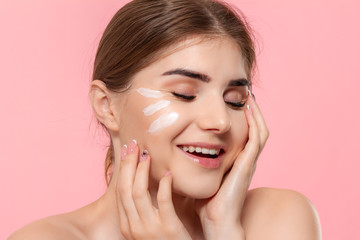 Obraz premium Beautiful model applyes moisturizing cosmetic product to skin holding white tube of a hyaluronic cream isolated over pink background. Concept of beauty and health treatment.
