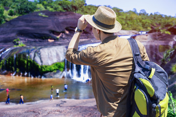 young man standing in front of waterfall , man traveler, with backpack,Beautiful waterfalls in Thailand,Travel and freedom.