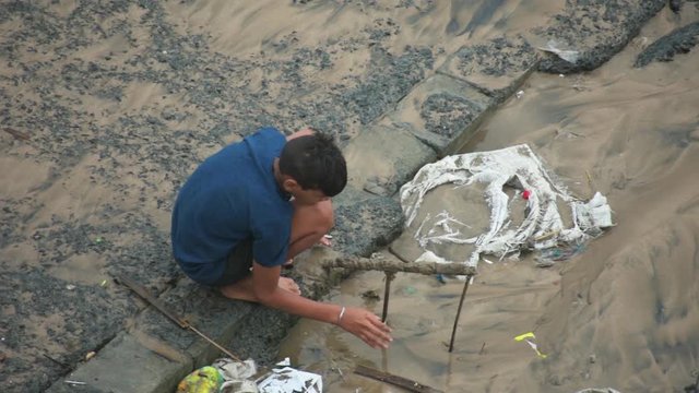 Typical village poor boy playing with mud near dirty beach  in spring. Enjoying life a joyful way in evening carefree rural life
