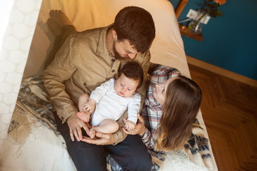 Lovely family of young parents and baby lying in bed at home