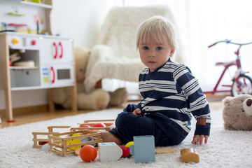 Sweet toddler boy, playing with teddy bears and wooden toys from kids kitchen set