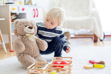 Sweet toddler boy, playing with teddy bears and wooden toys from kids kitchen set