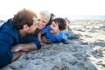 Young family with two small children lying down outdoors on beach.