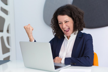 Happy excited businesswoman making winner gesture. Business woman using computer, looking at screen and shouting for joy. Good news or success concept