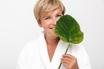 Image of happy adult woman with short blond hair wearing white housecoat holding green leaf