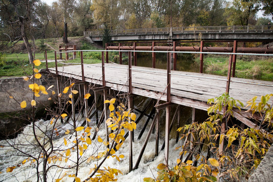 old wooden bridge over the river in the foreground yellow autumn leaves