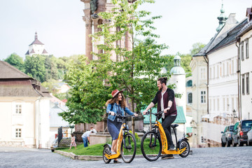Young tourist couple travellers with electric scooters in small town, talking.