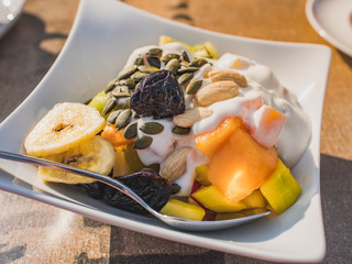 Healthy breakfast in hotel, top view, close-up. Elegante bowl with yogurt, dried fruit, nuts, seeds - fresh melon, pineapple, plum and banana dried fruit.