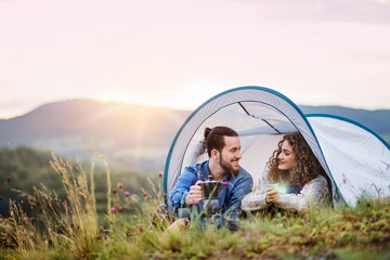 Young tourist couple travellers with tent shelter sitting in nature, drinking coffee.