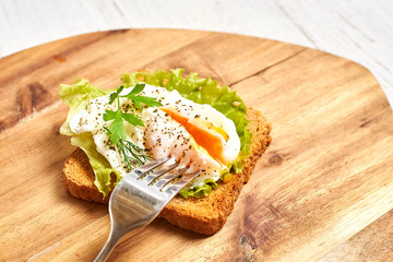 Poached egg, benedict on toasted white bread toast with salad and spices on a wooden background.