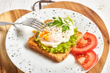 Fototapeta na wymiar Poached egg, benedict on toasted white bread toast with salad and spices on a plate on a light wooden background.