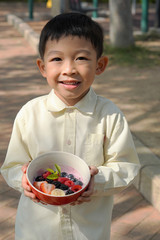 The cute happy Asian boy with the Acai/fruit salad bowl in his hands at the outdoor area.Kid eating...