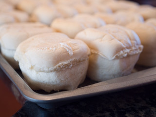 A close up of a tray full of pre-made uncooked or raw brown and serve style dinner rolls or buns on a non-stick baking sheet ready to be placed in the oven to bake for Thanksgiving dinner.