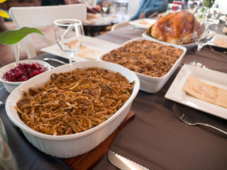 A view looking down across a beautiful Thanksgiving dinner table full of home made gourmet food including green bean casserole, sweet potatoes, cranberry sauce, turkey and place settings.