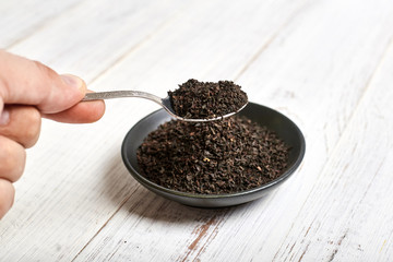 black dry tea in a spoon and clay bowl on a light wooden background.