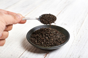 black dry tea in a spoon and clay bowl on a light wooden background.