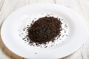 black dry tea on a white plate on a light wooden background.