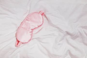 Silk pink eye mask lying on the white bedding in the morning,