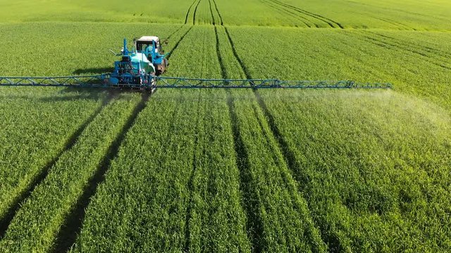 Aerial view of the tractor that irrigates the green field by special installation. The process of spraying field growths with pesticides and protection against insects of rodents, parasites and pests.