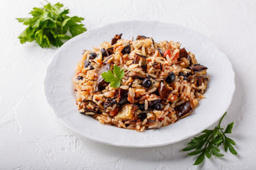 Eggplant pilaf served in white plate. Rice with aubergine,  black raisins and tomatoes on white table. Healthy vegetarian food concept.