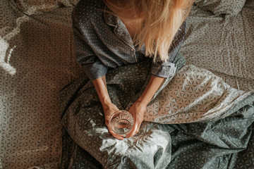 Woman in bed holding a glass of water in hand. Happy morning. Girl in pajamas. Healthy lifestyle, wellness. Proper nutrition. Drinking water. Morning with water. Sunlight on linens. Pillow, blanket