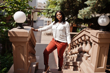 Formally dressed african american business woman in white blouse and red trousers. Successful dark...