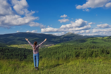 Fototapeta premium Young girl traveller standing in summer mountains with her hands raised