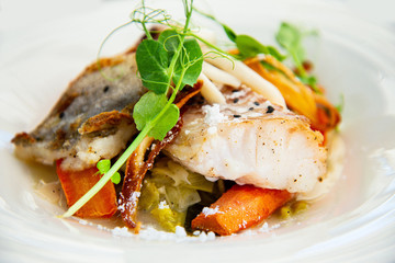 Delicious fillet of cod fish with carrots, leeks and mushrooms in white plate ready to be served