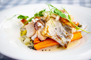 Delicious fillet of cod fish with carrots, leeks and mushrooms in white plate ready to be served