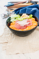 Japanese Chirashi made with assortment of three raw fishes, salmon, tuna and cod fish served on white vinegary rice with Wasabi sauce and ginger slices on top in a bowl.