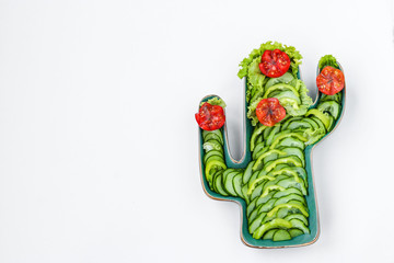 Green Cactus Shaped Dish with fresh salad of tomatoes, cucumbers and lettuce on white background: fiesta party, frida kahlo party, wild west party, horizontal orientation, top view, copy space