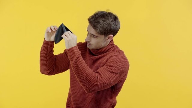poor man in sweater shaking empty wallet isolated on yellow