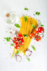 Traditional ingredients food  spaghetti pasta. Mediterranean italian dinner concept background. Dried pasta, garlic, olive oil, basil, tomatoes. White stone background. Top view with copy space.