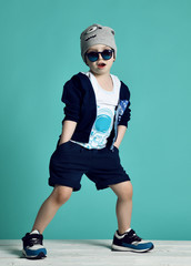 Cool kid boy in blue sunglasses hoody sneakers and headgear cool posing with his hands in pockets of his shorts
