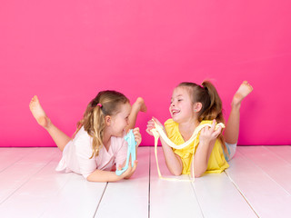 two beautiful girls playing with homemade slime and having a lot of fun in front of pink background