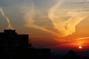 Urban silhouette with colorful sky covered in contrails and clouds during sunrise.