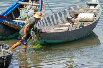 Man fishing with stick surrounded by colourful boats, Vietnam