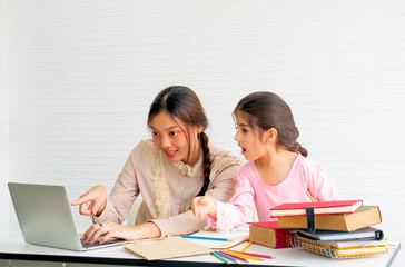 Pretty teen girl point to laptop screen and her younger sister look feel surprise in front of white curtain.