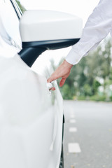 Close-up of man opening the door of his new white car outdoors